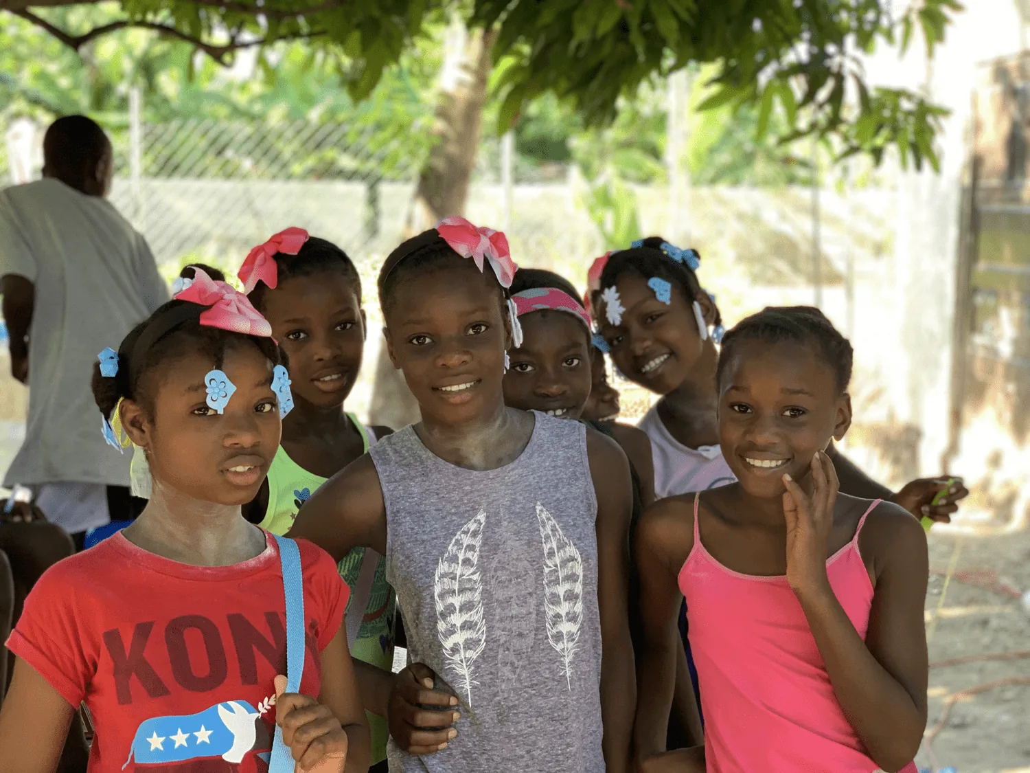 Girls in bright bows smiling under the mango tree at the Nehemiah's Children home